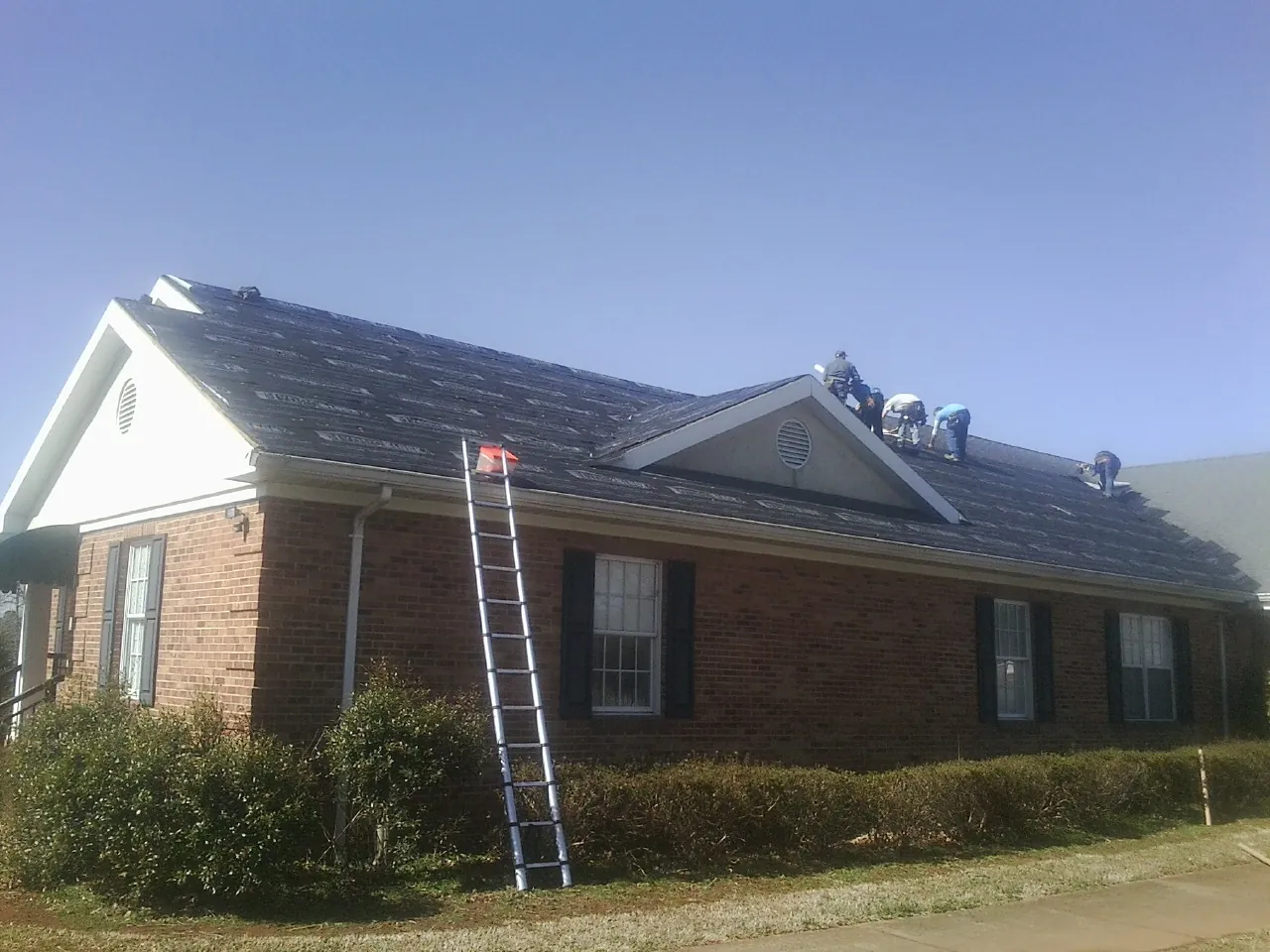 Crew tearing shingles off a brick ranch roof with a ladder set — Metal Roof Repair work by our crew in Hartville