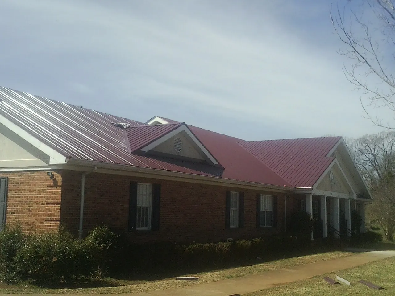 Red metal roof with gabled entries on a long brick building, from a Hail Damage Roof Repair job in Hartville