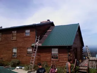 Green metal roof going on a two story log home with ladders set in Hartville