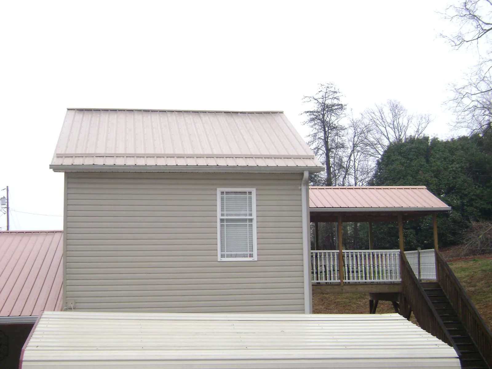 Tan metal roofs on a two story addition and attached porch, from a Roof Replacement job in Hartville